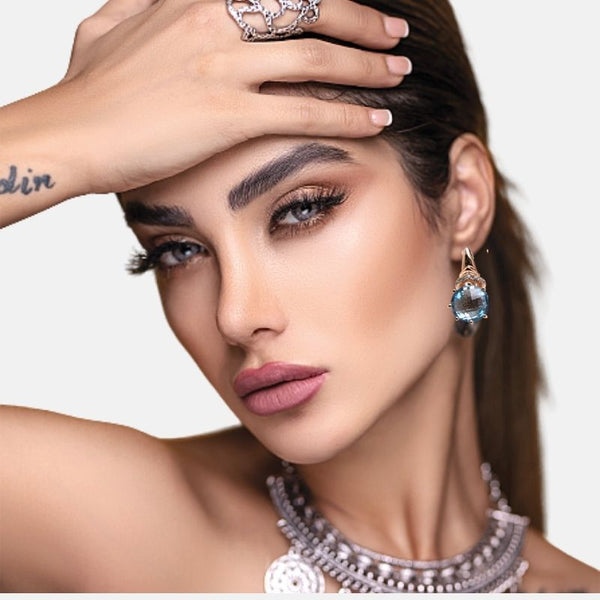 Boucles d'oreilles pierre topaze bleu ciel sur un visage de femme brune cheveux longs